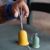 A close up of the yellow wooden Grapat jingle joy bells hanging on a child's finger