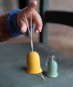 A close up of the yellow wooden Grapat jingle joy bells hanging on a child's finger