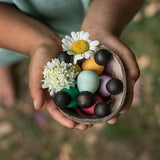 Close up of hands holding the Grapat dark baby nin peg doll toys in a wooden bowl with a white flower