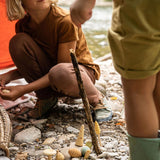 Girl crouched down on some sandy pebbles playing with the Grapat plastic-free wooden wonders toy set