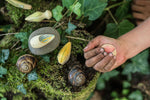 Close up of a childs hand holding a Grapat eco-friendly wooden wild creature toy above some dark green leaves