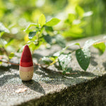 Close up of a Grapat yay open ended wooden play figure stood on a stone wall next to a green leaf