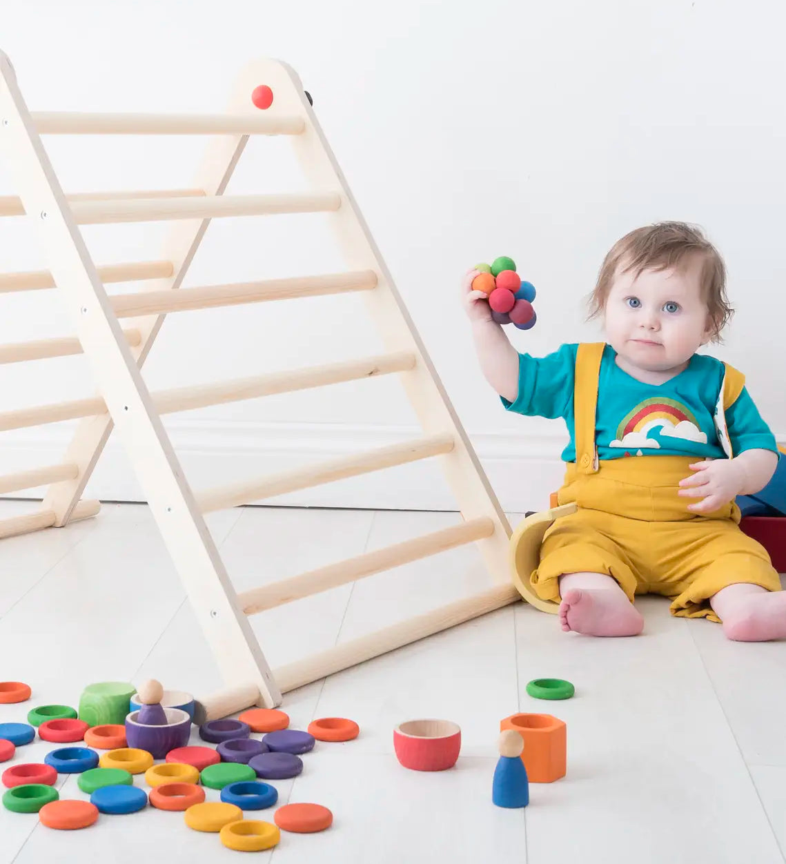 Small toddler playing with Grapat handcrafted loose coins and rings in rainbow colours next to a Triclimb climbing frame