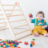 Small toddler playing with Grapat handcrafted loose coins and rings in rainbow colours next to a Triclimb climbing frame