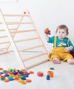 Small toddler playing with Grapat handcrafted loose coins and rings in rainbow colours next to a Triclimb climbing frame