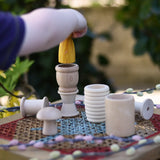 Grapat natural loose parts placed on a stool outdoors. Child placing a Grapat yellow peg doll in a mate. 