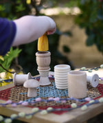 Grapat natural loose parts placed on a stool outdoors. Child placing a Grapat yellow peg doll in a mate. 