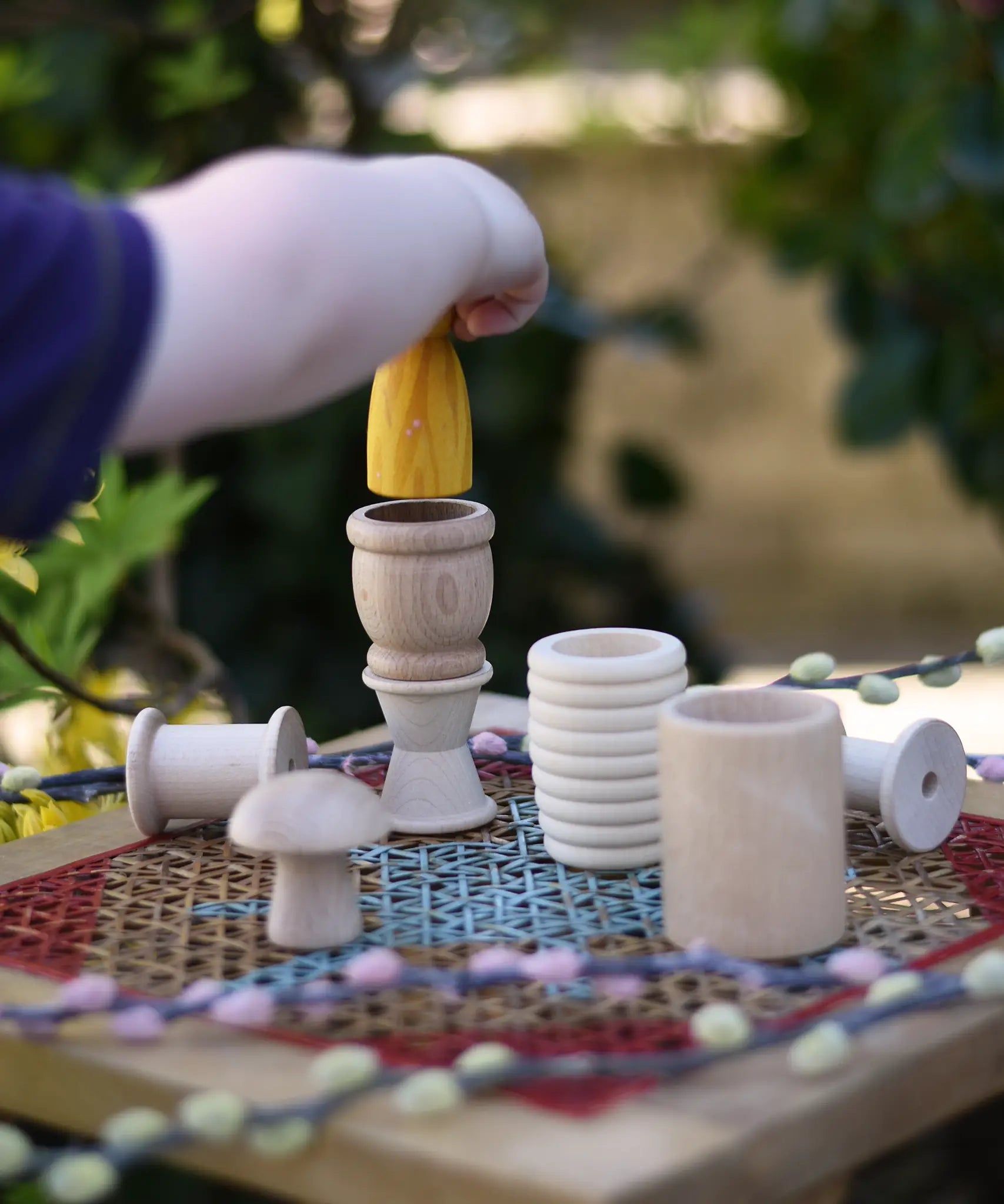 Grapat natural loose parts placed on a stool outdoors. Child placing a Grapat yellow peg doll in a mate. 