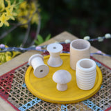 Grapat natural wooden loose parts placed on a yellow dish on a stool outdoors. 