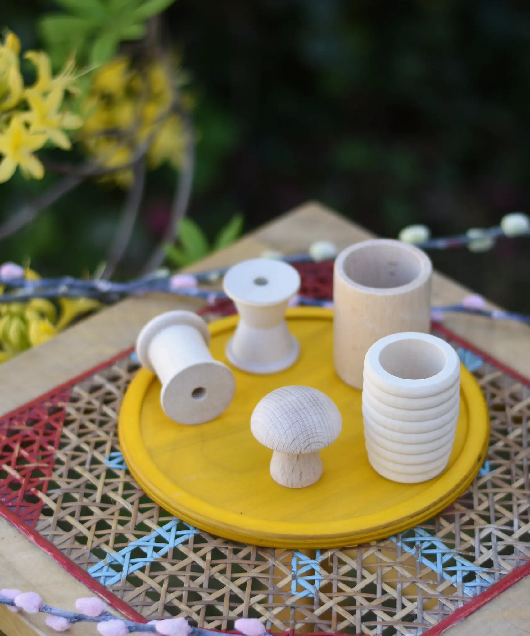 Grapat natural wooden loose parts placed on a yellow dish on a stool outdoors. 