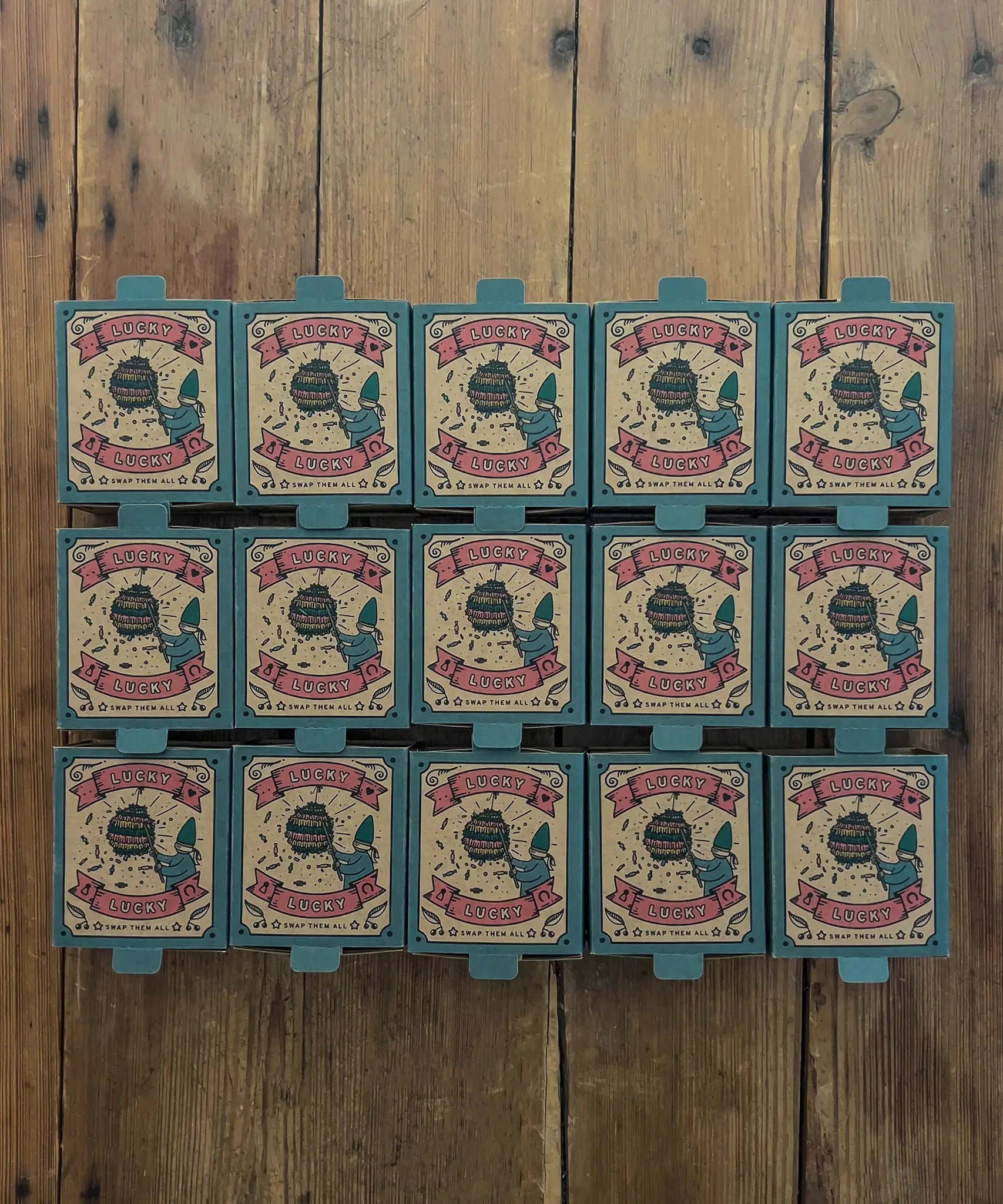 15 boxes of Grapat Lucky Lucky boxes mystery toy boxes lined up on a wooden floor with the surprise wooden toys hidden inside.