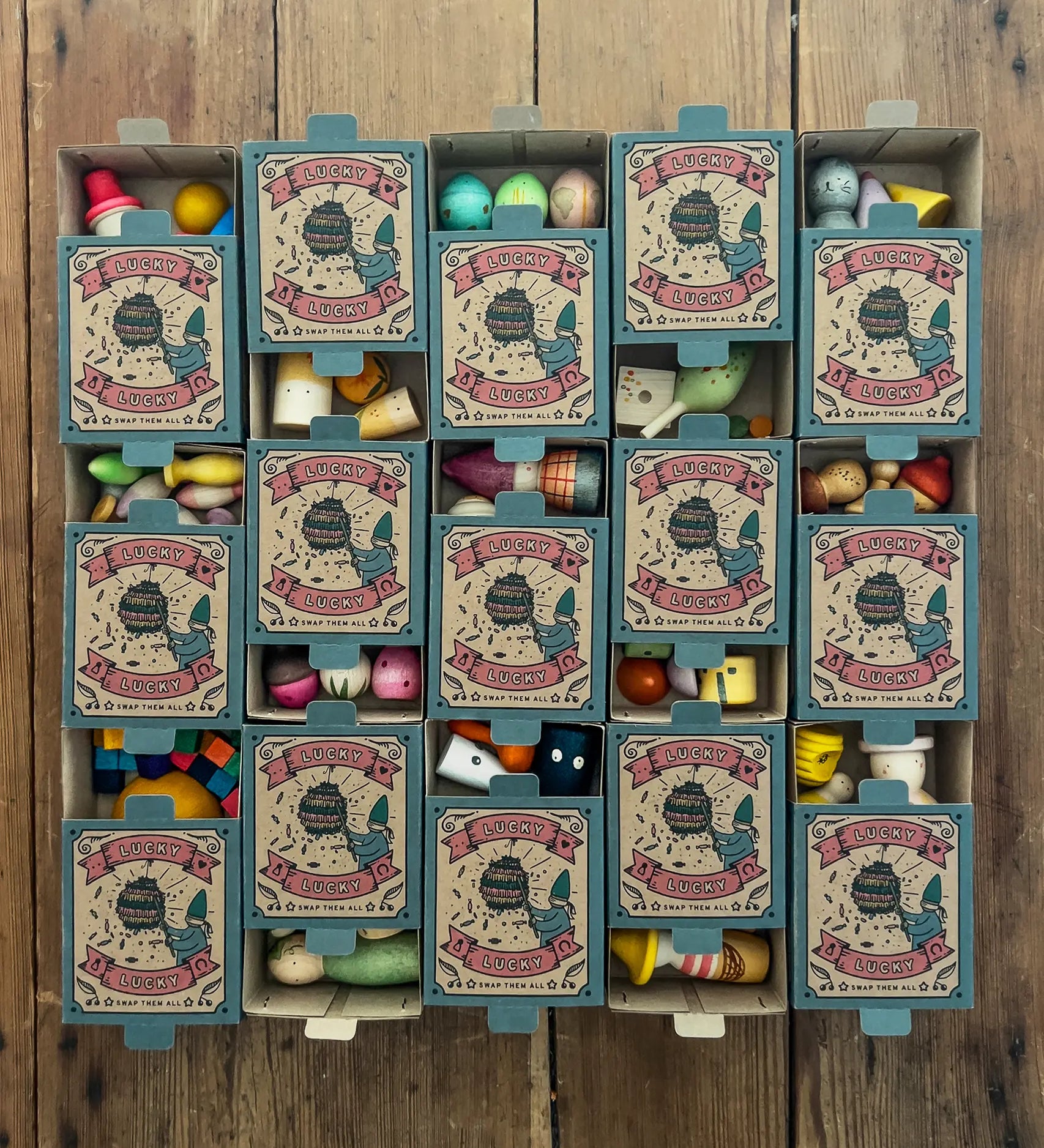15 boxes of Grapat Lucky Lucky boxes mystery toy boxes lined up and slightly open showing a peek at the wooden toys inside.