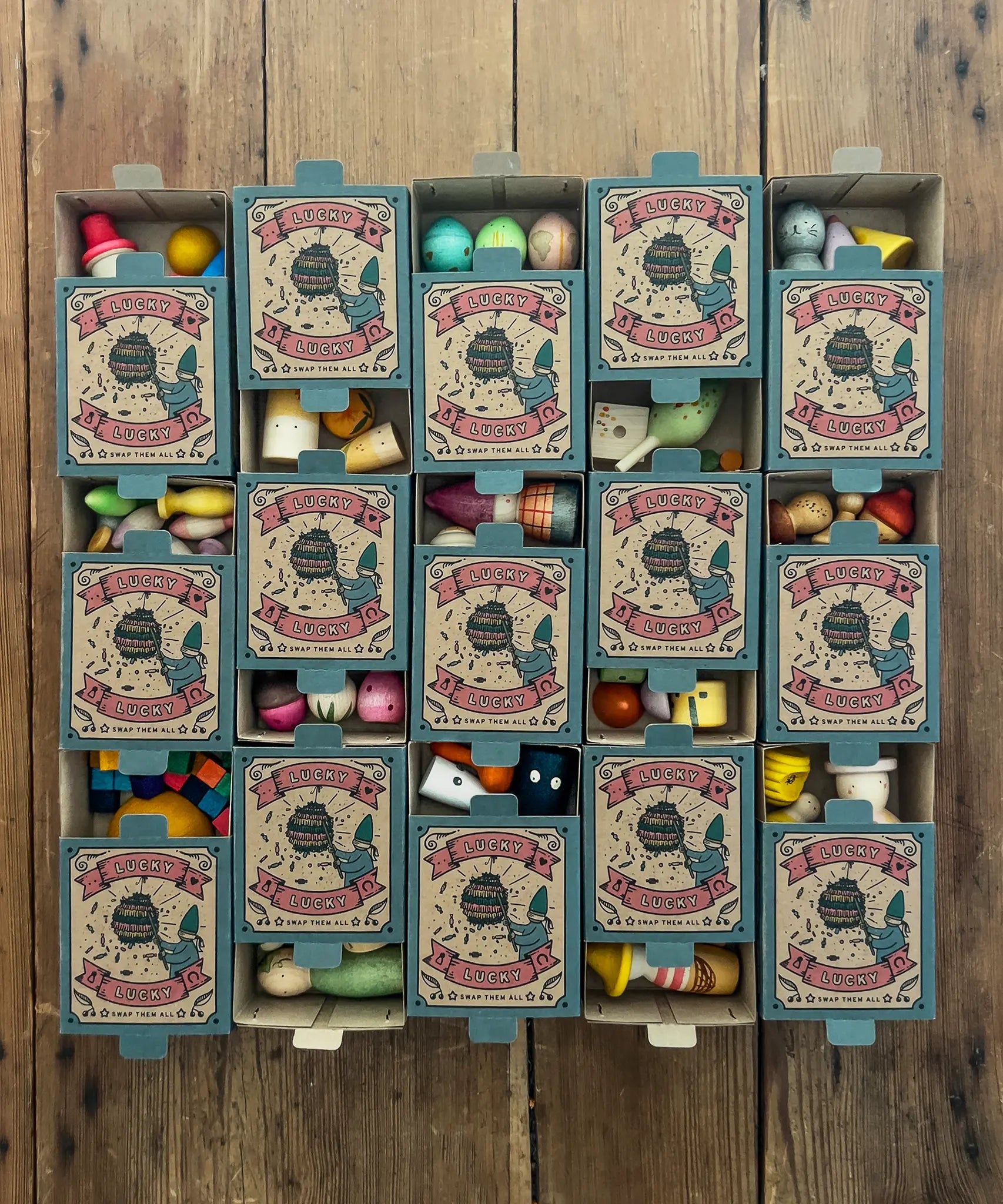 15 boxes of Grapat Lucky Lucky boxes mystery toy boxes lined up and slightly open showing a peek at the wooden toys inside.