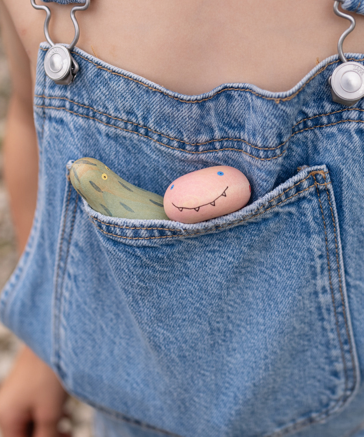 A close up of the wooden monster inspired peg dolls from the Grapat lucky lucky box sitting in a pocket showing the delicate and playful painted detail