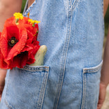 A close up of the wooden monster peg dolls from the Grapat lucky lucky box in a pocket next to a red flower showing the delicate and playful hand painted design 