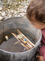 A close up of the 3 swimming inspired wooden peg dolls and pieces from the Grapat lucky lucky boxes in a bucket of water with a homemade raft on the water