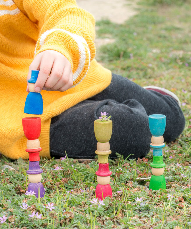 A child stacking the Grapat 12 Magos wooden peg dolls with top hats in a rainbow of 12 colours. These wooden toys are part of a wide range of open ended toys available at Babipur.  