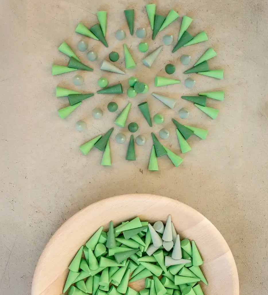 Green Grapat wooden cone pieces in a pattern next to a bowl of other loose cones