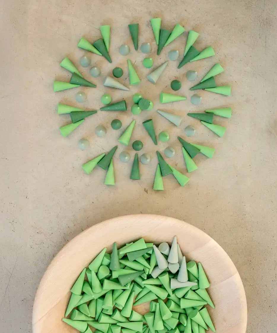 Green Grapat wooden cone pieces in a pattern next to a bowl of other loose cones