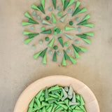 Green Grapat wooden cone pieces in a pattern next to a bowl of other loose cones