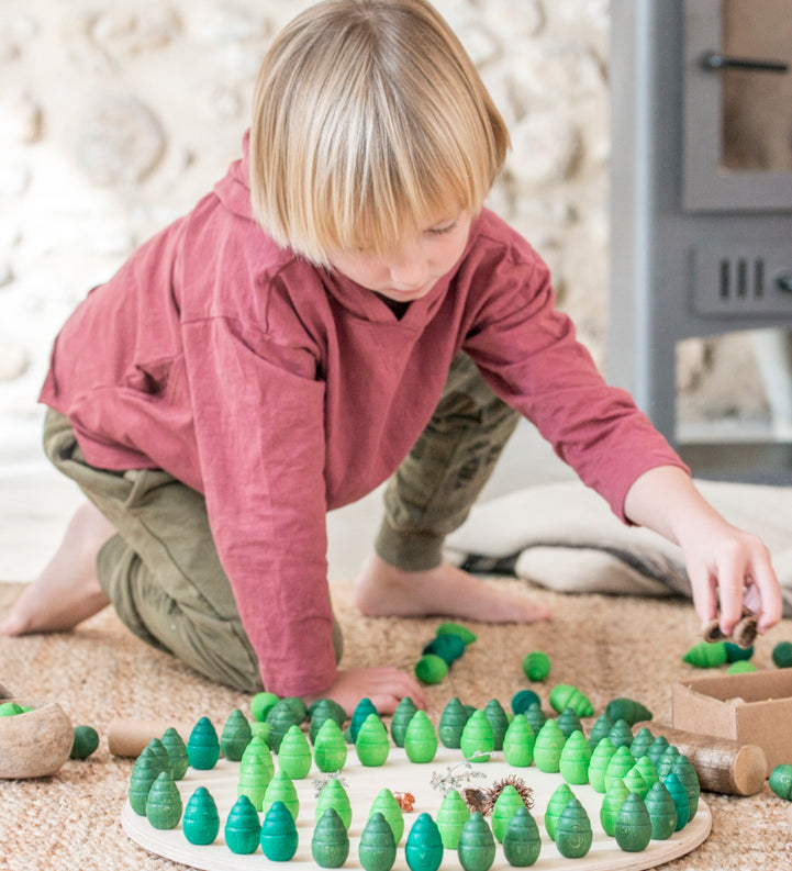 A child playing with the Grapat 36 Mandala Pieces Little Trees. 36 tree shaped mandala pieces in 3 different shades of green, 12 in each colour. Grapat have a wide range of wooden toys and loose parts available at Babipur. 
