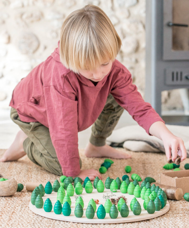 A child playing with the Grapat 36 Mandala Pieces Little Trees. 36 tree shaped mandala pieces in 3 different shades of green, 12 in each colour. Grapat have a wide range of wooden toys and loose parts available at Babipur. 