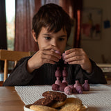 A child playing with the Grapat 36x Mandala Pineapples, stacking the pieces on top of each other. 36 pineapple shaped mandala pieces in three shades of purple, 12 in each colour. Grapat have a wide range of wooden toys and loose parts available at Babipur. 