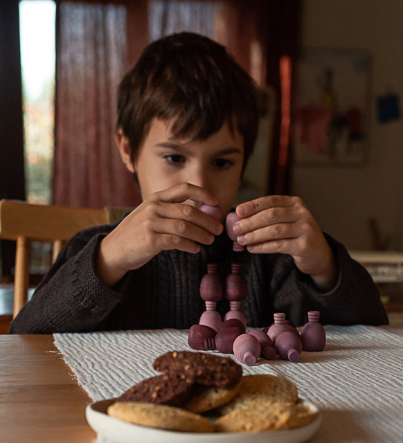 A child playing with the Grapat 36x Mandala Pineapples, stacking the pieces on top of each other. 36 pineapple shaped mandala pieces in three shades of purple, 12 in each colour. Grapat have a wide range of wooden toys and loose parts available at Babipur. 