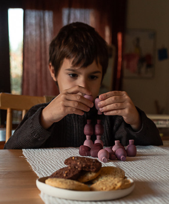 A child playing with the Grapat 36x Mandala Pineapples, stacking the pieces on top of each other. 36 pineapple shaped mandala pieces in three shades of purple, 12 in each colour. Grapat have a wide range of wooden toys and loose parts available at Babipur. 