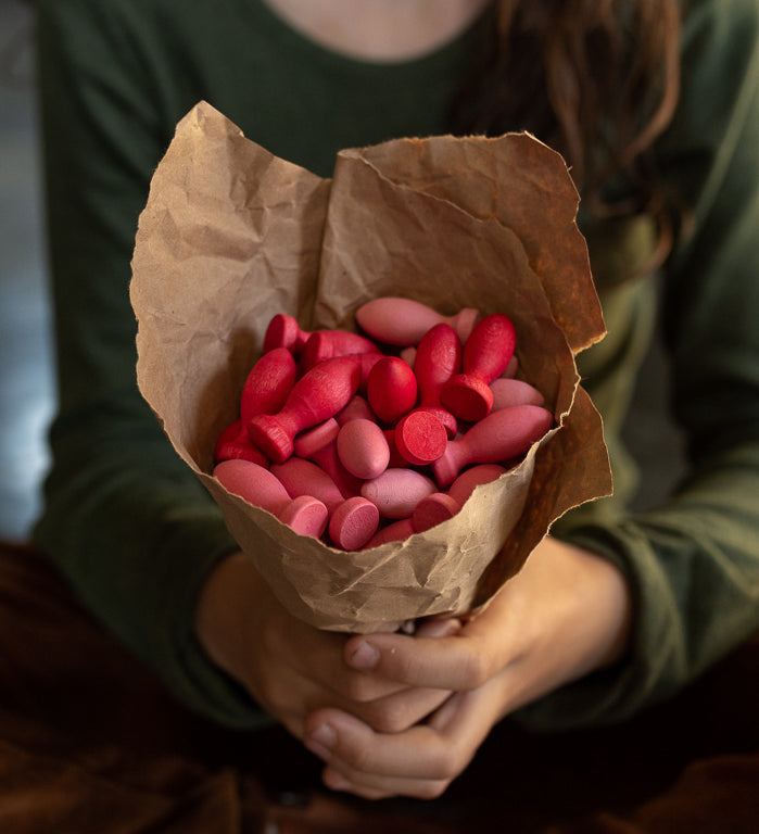 A set of Grapat 36x Mandala Flower Petals placed in brown paper held in a child's hand. A set of 36 flower petal mandala pieces in three shades of pink. Grapat have a wide range of wooden toys and loose parts available at Babipur. 