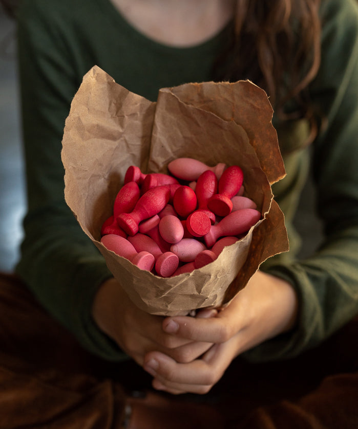 A set of Grapat 36x Mandala Flower Petals placed in brown paper held in a child's hand. A set of 36 flower petal mandala pieces in three shades of pink. Grapat have a wide range of wooden toys and loose parts available at Babipur. 