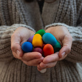Some eggs from the Grapat 36x Mandala Rainbow Eggs set shown in an adult's hands. A set of 36 wooden egg shaped pieces in a range of 12 colours. Grapat have a wide range of wooden toys and loose parts available at Babipur. 