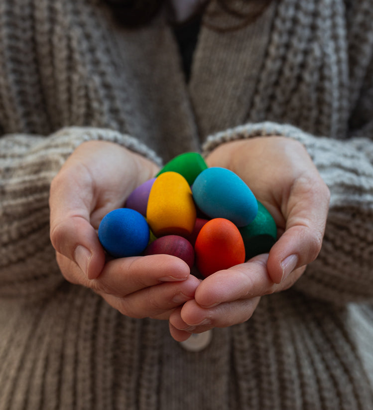 Some eggs from the Grapat 36x Mandala Rainbow Eggs set shown in an adult's hands. A set of 36 wooden egg shaped pieces in a range of 12 colours. Grapat have a wide range of wooden toys and loose parts available at Babipur. 