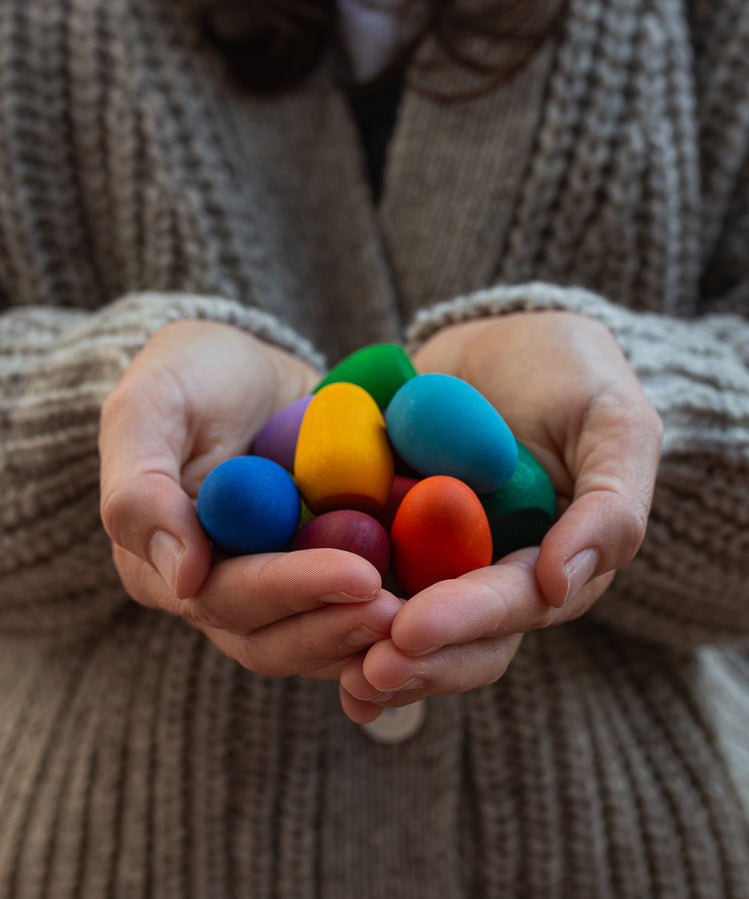 Some eggs from the Grapat 36x Mandala Rainbow Eggs set shown in an adult's hands. A set of 36 wooden egg shaped pieces in a range of 12 colours. Grapat have a wide range of wooden toys and loose parts available at Babipur. 