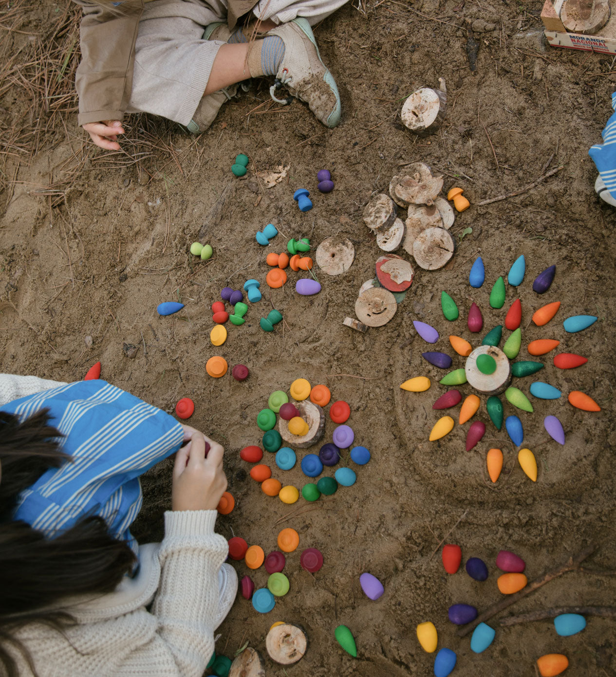 Children on a beach creating mandalas with rainbow coloured, snowflake mandala pieces.