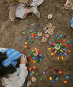 Children on a beach creating mandalas with rainbow coloured, snowflake mandala pieces.