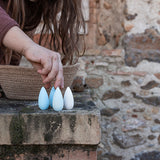 A child's hand going to pick up a Grapat Mandala Snowflake. 36 snowflake shaped wooden loose parts in 2 shades of blue and white, 12 of each colour. Grapat have a wide range of wooden toys and loose parts available at Babipur. 