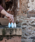 A child's hand going to pick up a Grapat Mandala Snowflake. 36 snowflake shaped wooden loose parts in 2 shades of blue and white, 12 of each colour. Grapat have a wide range of wooden toys and loose parts available at Babipur. 