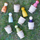 Grapat mates wooden loose part cups with animal crew peg dolls placed inside placed on grass.