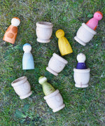 Grapat mates wooden loose part cups with animal crew peg dolls placed inside placed on grass.