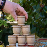 Grapat 6 mates wooden loose parts stacked up on a stool outdoors, adult's hand reaching for the top mate.
