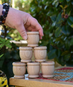 Grapat 6 mates wooden loose parts stacked up on a stool outdoors, adult's hand reaching for the top mate.