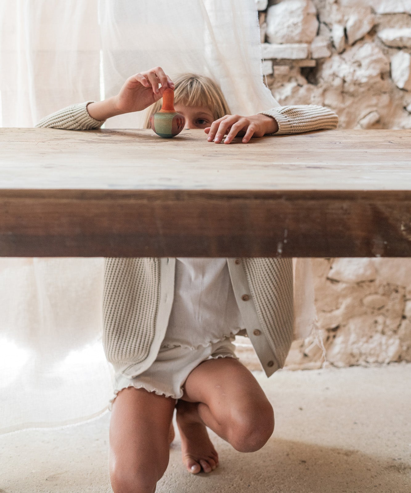 Child playing with the Grapat wooden mellow orange wobble wooden bird on a wooden table showing the hand painted pink and purple detailing. 