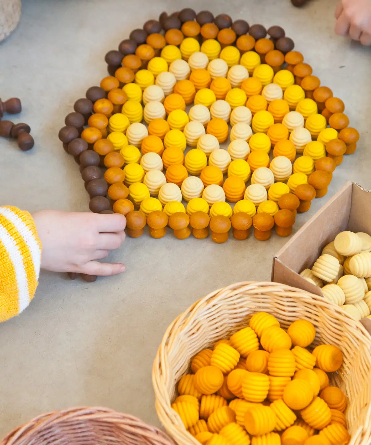 Child sorting Grapat handcrafted mini wooden honeycomb pieces into a pentagon shape on a concrete surface