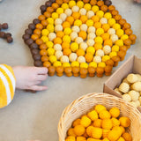 Child sorting Grapat handcrafted mini wooden honeycomb pieces into a pentagon shape on a concrete surface