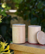 Two Grapat natural cups with lids on a stool outdoors. 