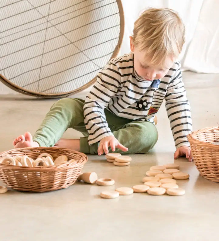 Child playing with Grapat's natural handcrafted wooden disks on a concrete floor