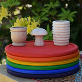 Grapat loose parts, mates, mushroom, honeycomb cup placed on a stack of rainbow dishes. 