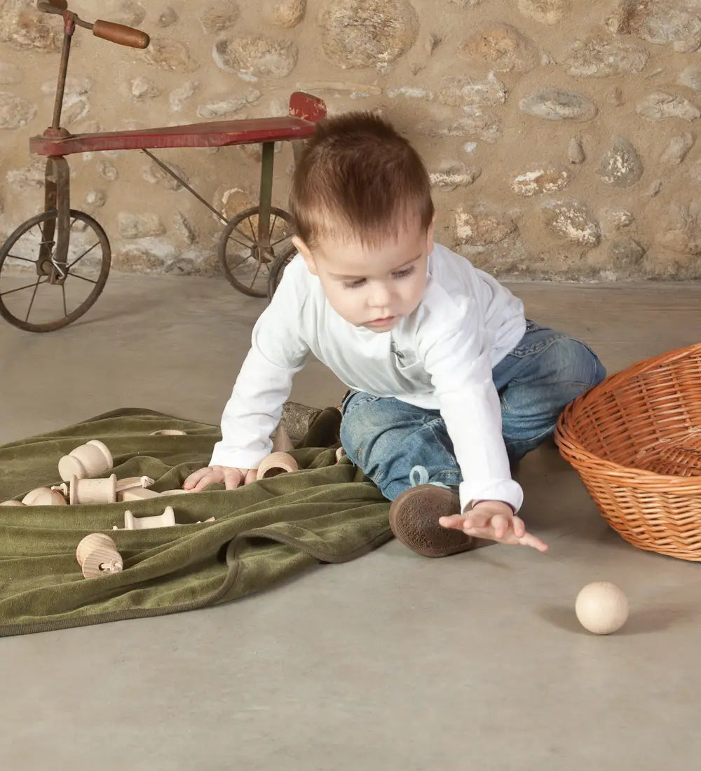 Child playing with a Grapat natural handcrafted wooden ball on a concrete surface