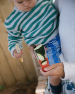 A child sorting various seeds and food items whilst holding onto one of the Grapat Wooden Sensory Play Tools. Different foods lay on the table which is covered in a blue and white chequred table cloth